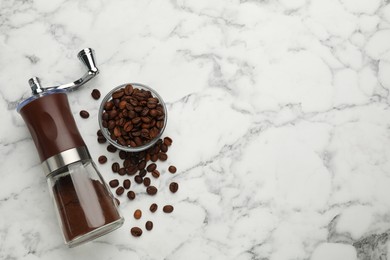 Manual coffee grinder with powder and beans on white marble table, flat lay. Space for text