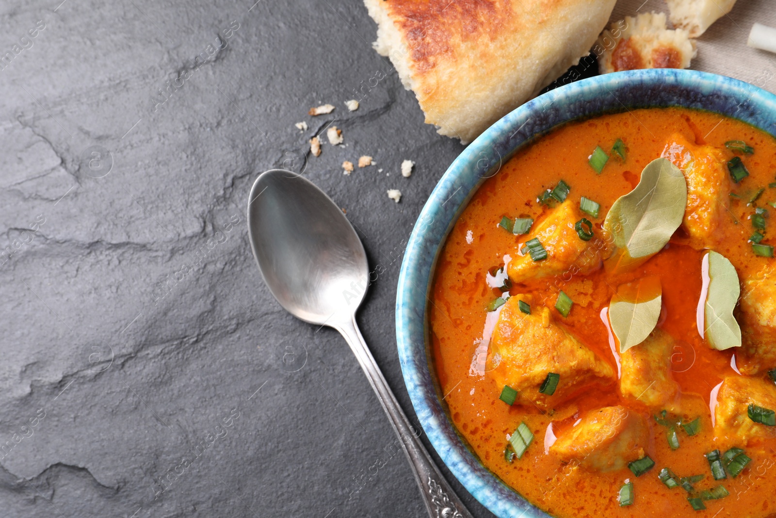 Photo of Bowl of delicious chicken curry on black table, flat lay. Space for text