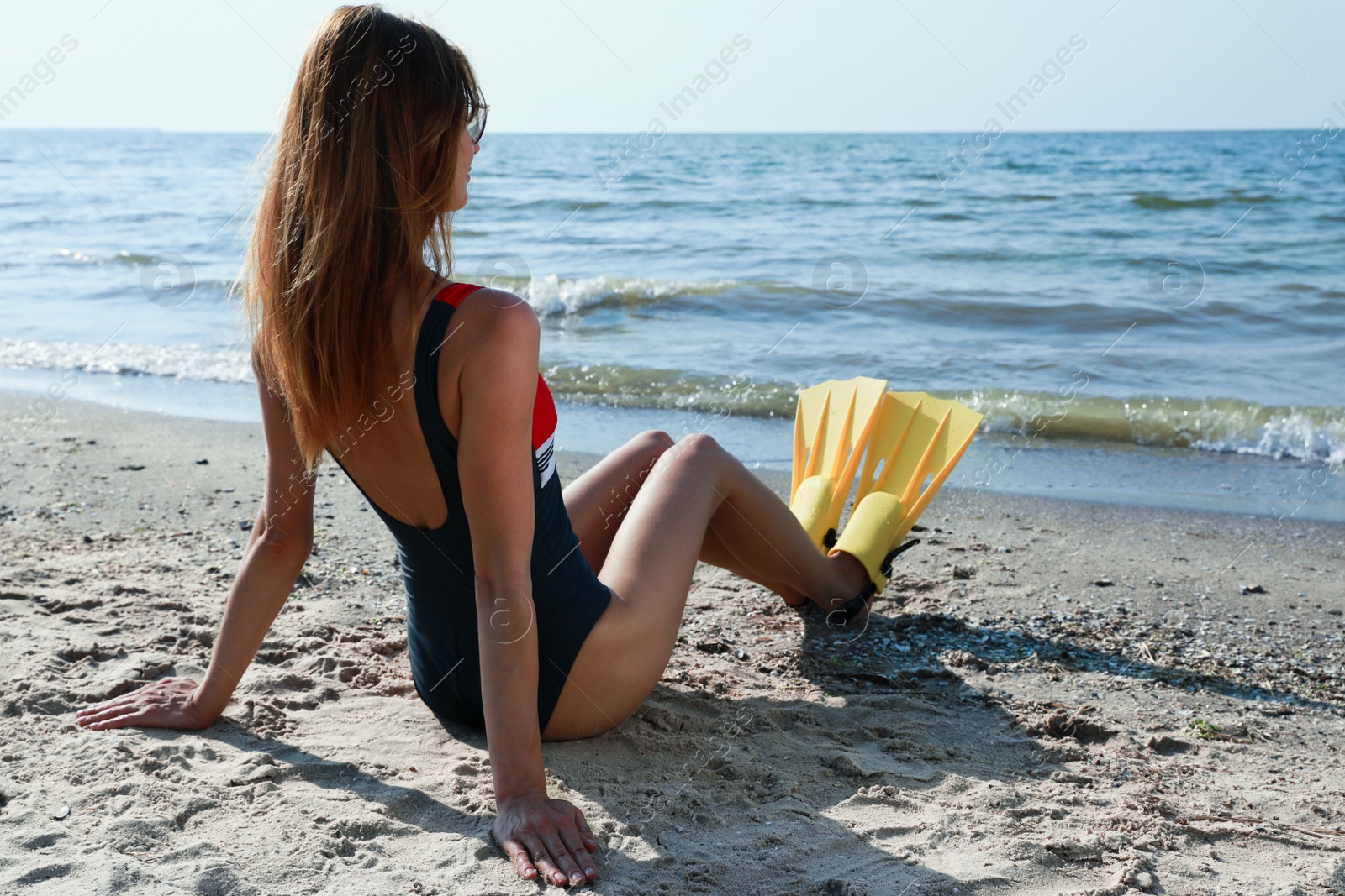 Photo of Woman in flippers sitting near sea on beach, back view