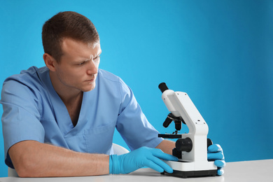 Photo of Scientist using modern microscope at table against blue background. Medical research