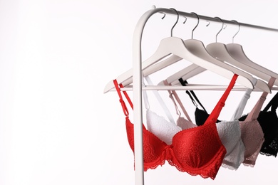 Hangers with beautiful lace bras on rack against white background. Stylish underwear