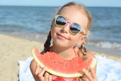 Photo of Cute little girl with sunglasses eating juicy watermelon on beach