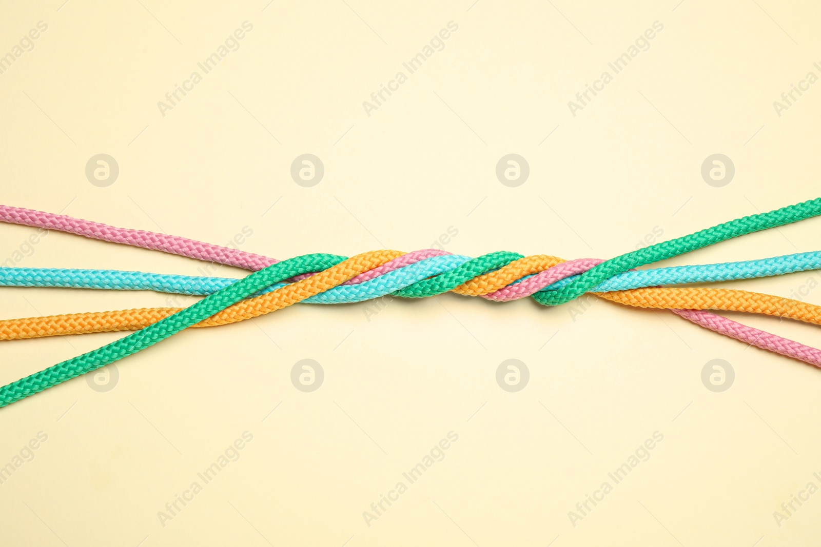 Photo of Twisted colorful ropes on beige background, top view. Unity concept