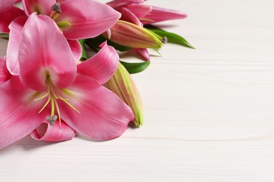 Beautiful pink lily flowers on white wooden table, closeup. Space for text