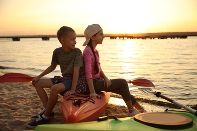 Photo of Happy children sitting on kayak near river at sunset. Summer camp