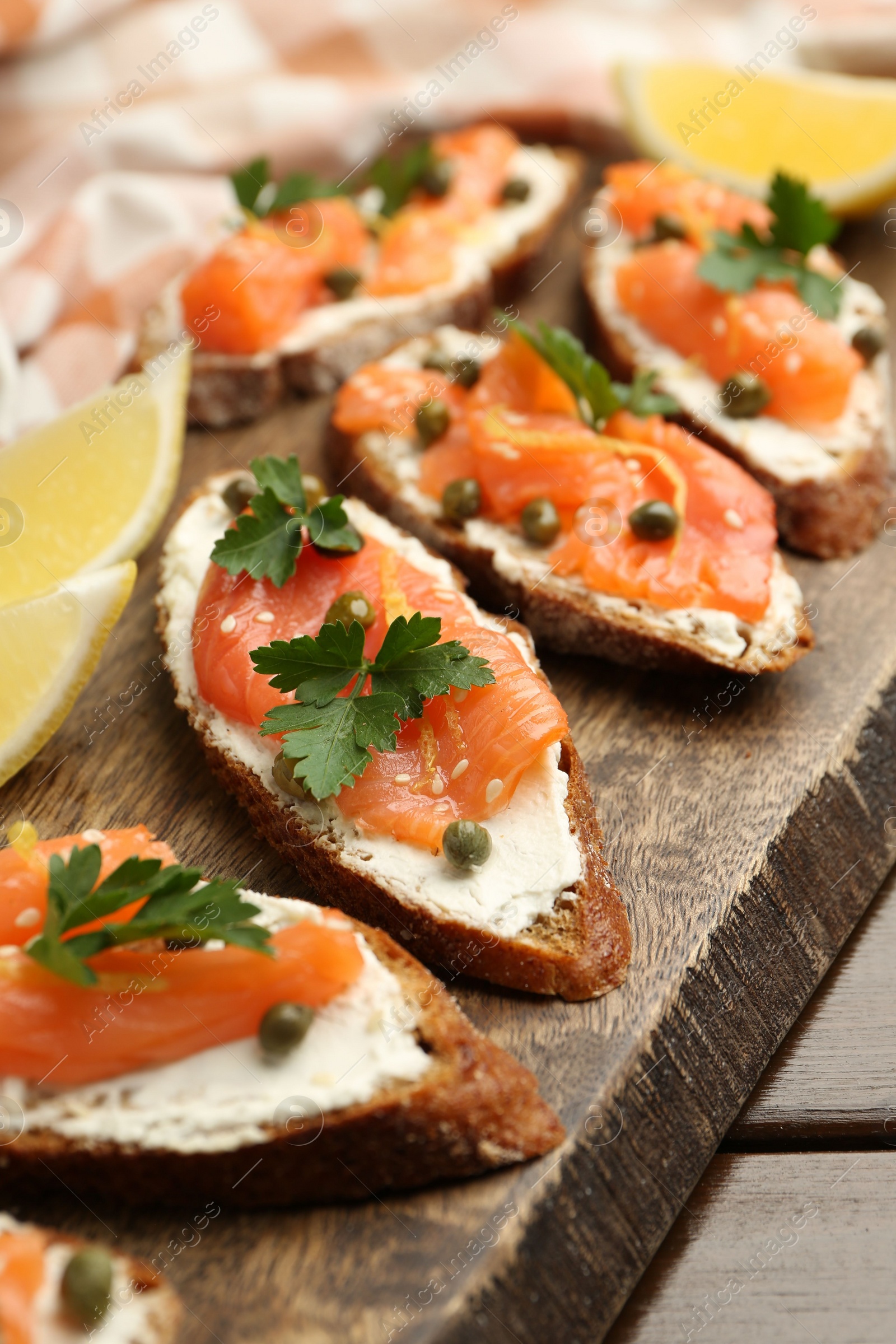 Photo of Tasty canapes with salmon, capers, lemon and cream cheese on wooden table, closeup