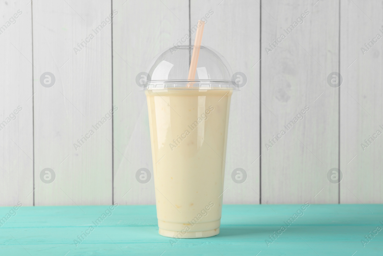 Photo of Tasty smoothie in plastic cup on light blue table against white wooden wall