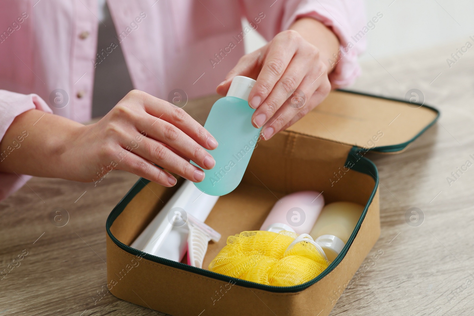 Photo of Woman packing cosmetic travel kit into compact toiletry bag at wooden table, closeup. Bath accessories