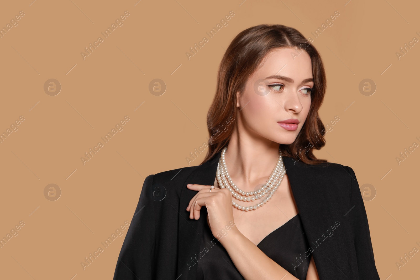 Photo of Young woman wearing elegant pearl jewelry on brown background, space for text