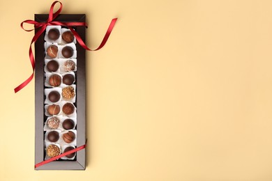 Box with delicious chocolate candies on beige table, top view. Space for text