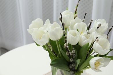 Beautiful bouquet of willow branches and tulips in vase on table indoors, space for text