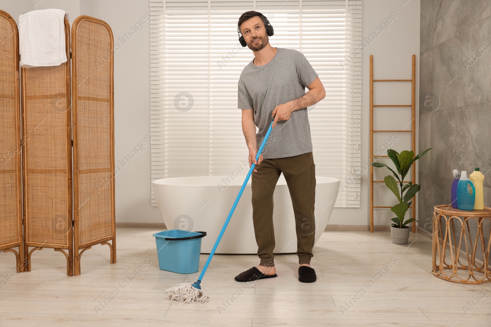 Photo of Enjoying cleaning. Man in headphones listening to music and mopping floor in bathroom