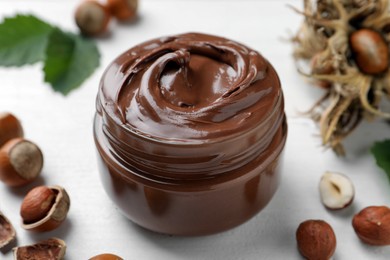 Glass jar with tasty chocolate spread and hazelnuts on white wooden table