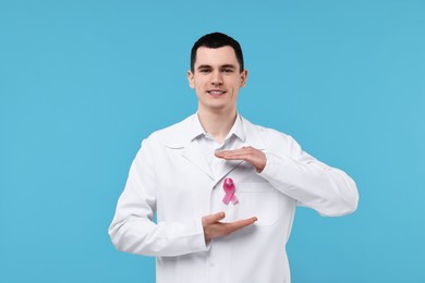 Photo of Portrait of smiling mammologist protecting pink ribbon on light blue background. Breast cancer awareness