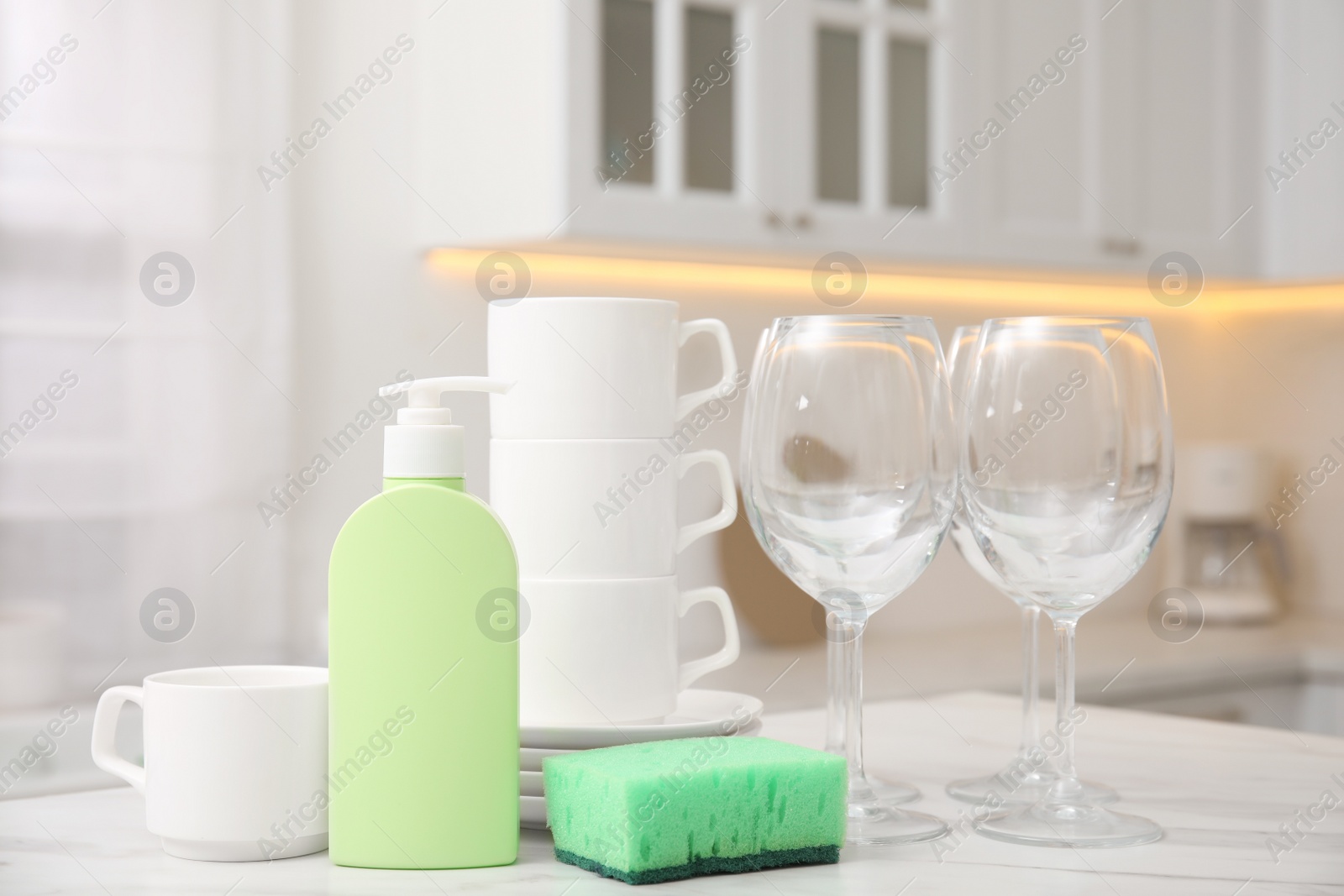 Photo of Clean glasses, cups and cleaning product on table in stylish kitchen