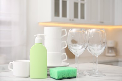 Photo of Clean glasses, cups and cleaning product on table in stylish kitchen