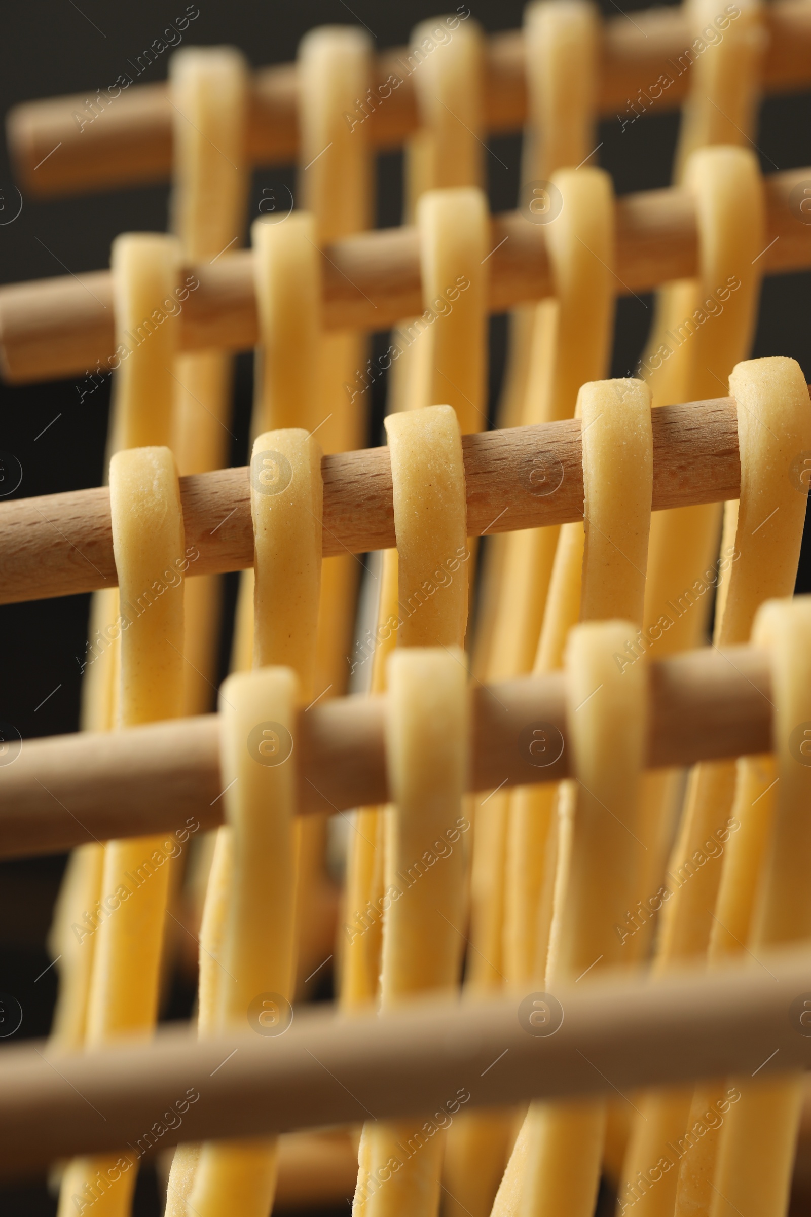 Photo of Homemade pasta drying on wooden rack against dark background, closeup