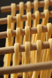 Photo of Homemade pasta drying on wooden rack against dark background, closeup