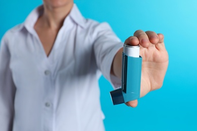 Photo of Female doctor holding asthma inhaler on color background, closeup. Medical object