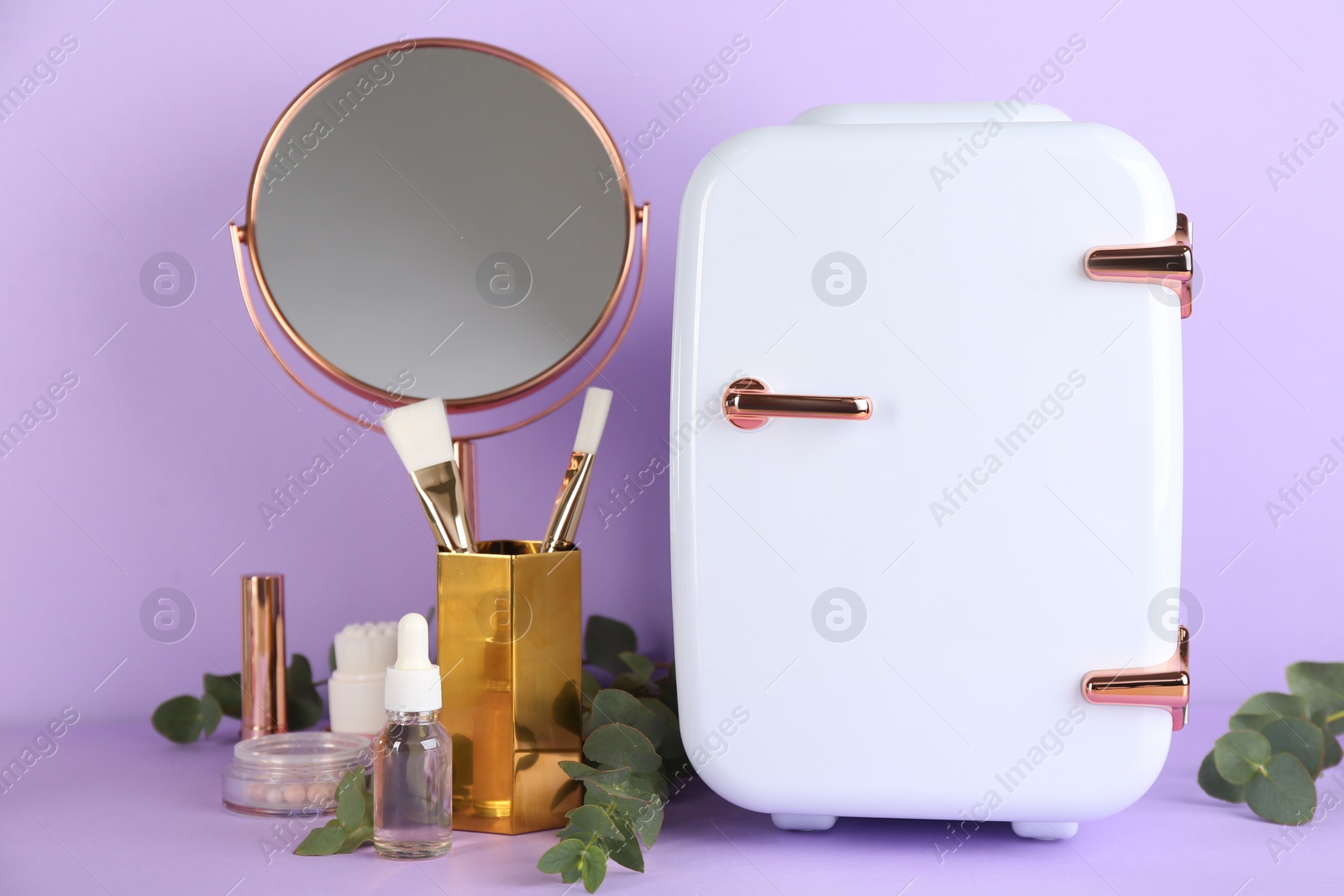 Photo of Cosmetic refrigerator and skin care products on violet background