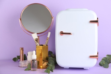 Cosmetic refrigerator and skin care products on violet background