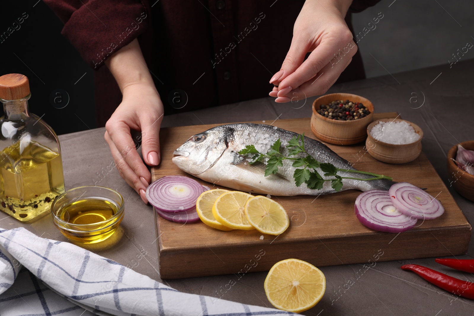 Photo of Woman salting raw dorado fish at grey table, closeup