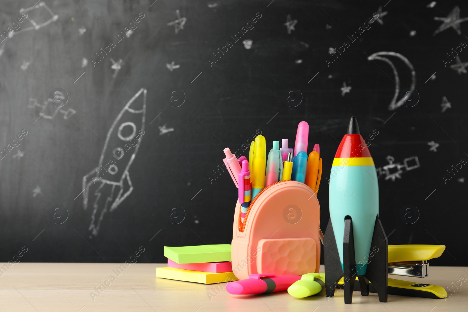 Photo of Bright toy rocket and school supplies on wooden table. Space for text