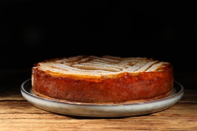Photo of Tasty apricot pie with powdered sugar on wooden table against dark background, closeup