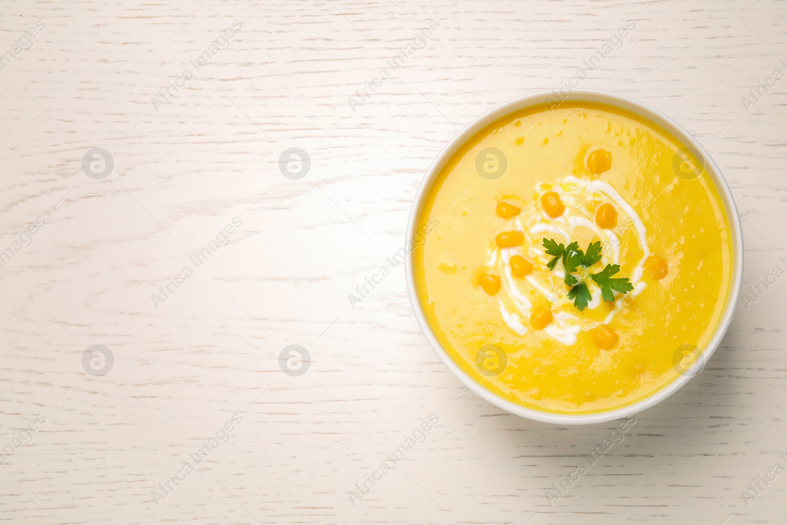 Photo of Delicious creamy corn soup served on white wooden table, top view. Space for text