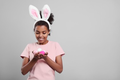 Photo of Happy African American woman in bunny ears headband with Easter egg on gray background, space for text