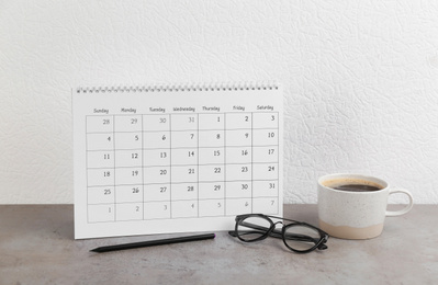 Photo of Calendar, glasses, pencil and cup of coffee on grey stone table