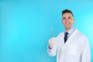 Photo of Male dentist holding professional tools on color background. Space for text
