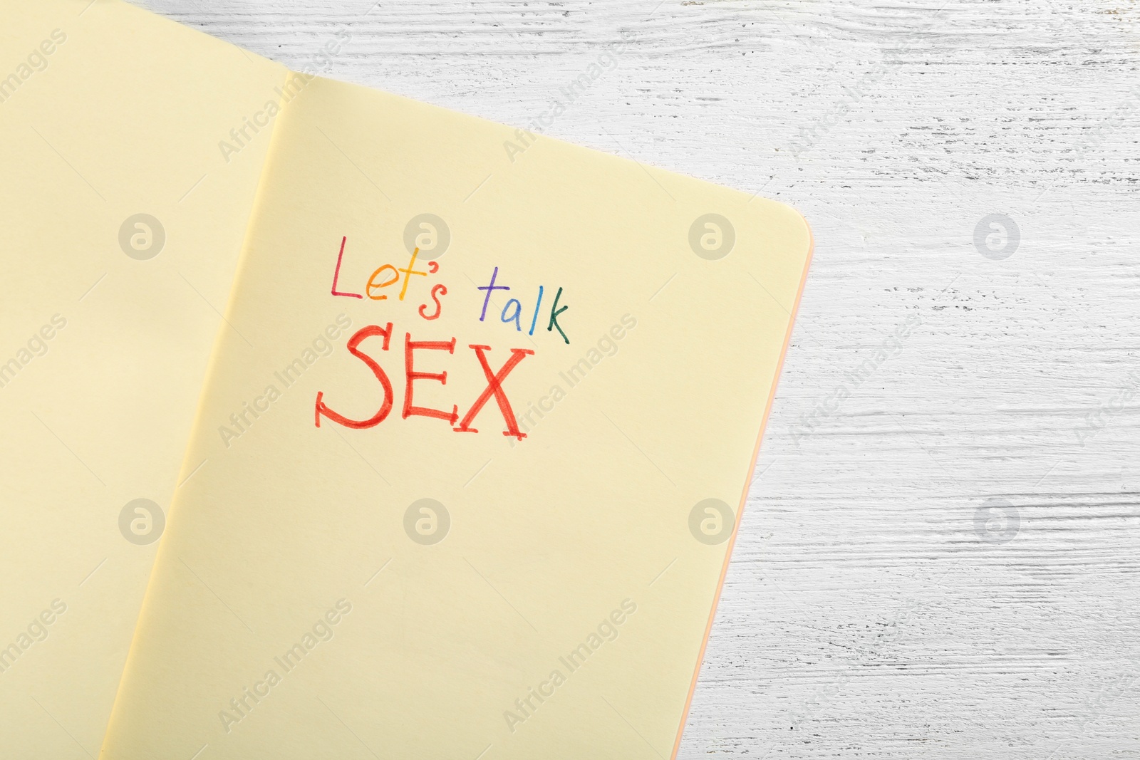 Photo of Notebook with phrase "LET'S TALK SEX" on white wooden background, top view