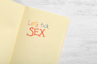 Photo of Notebook with phrase "LET'S TALK SEX" on white wooden background, top view