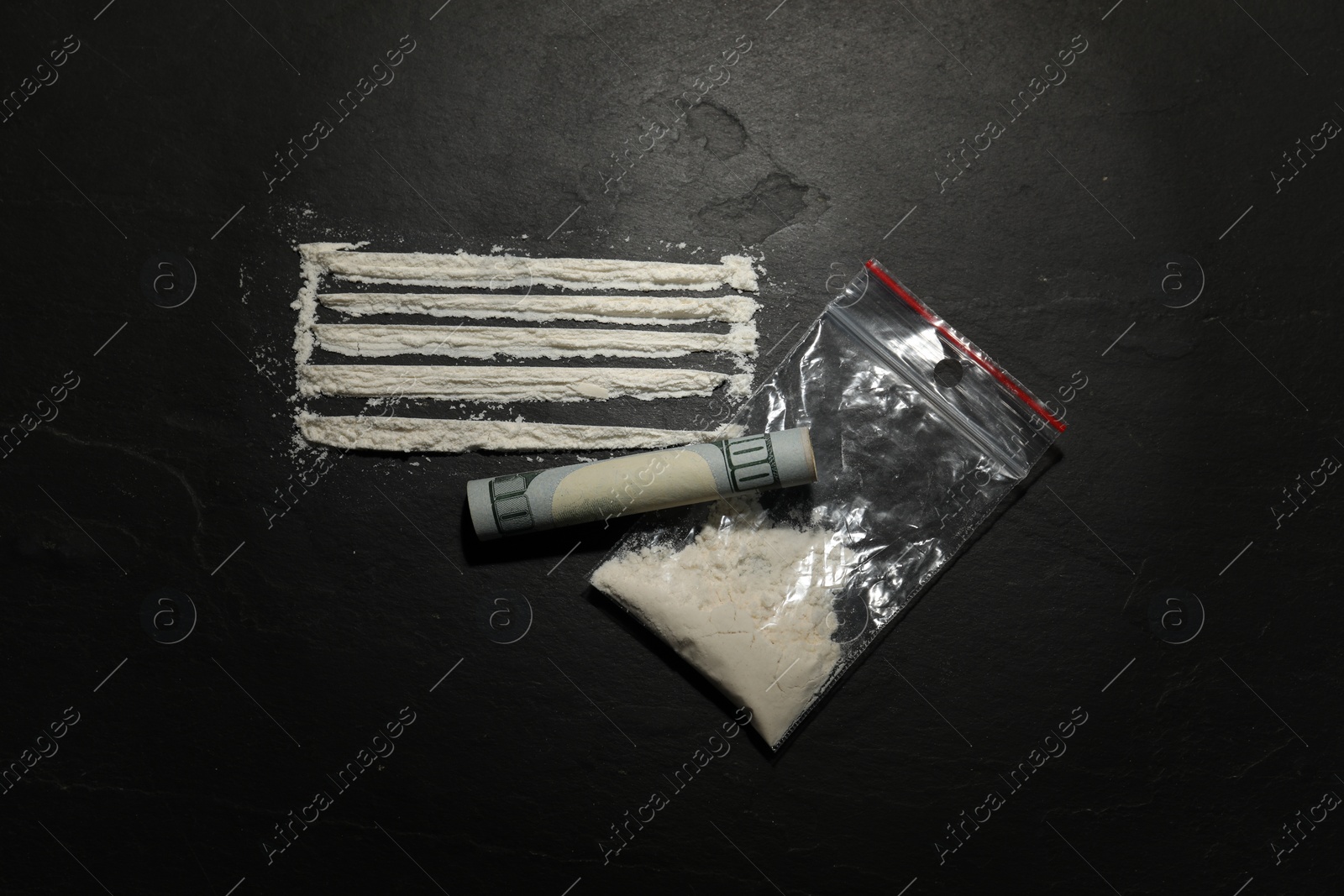 Photo of Drug addiction. Plastic bag with cocaine and rolled dollar banknote on dark textured background, flat lay