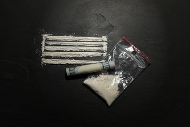 Photo of Drug addiction. Plastic bag with cocaine and rolled dollar banknote on dark textured background, flat lay