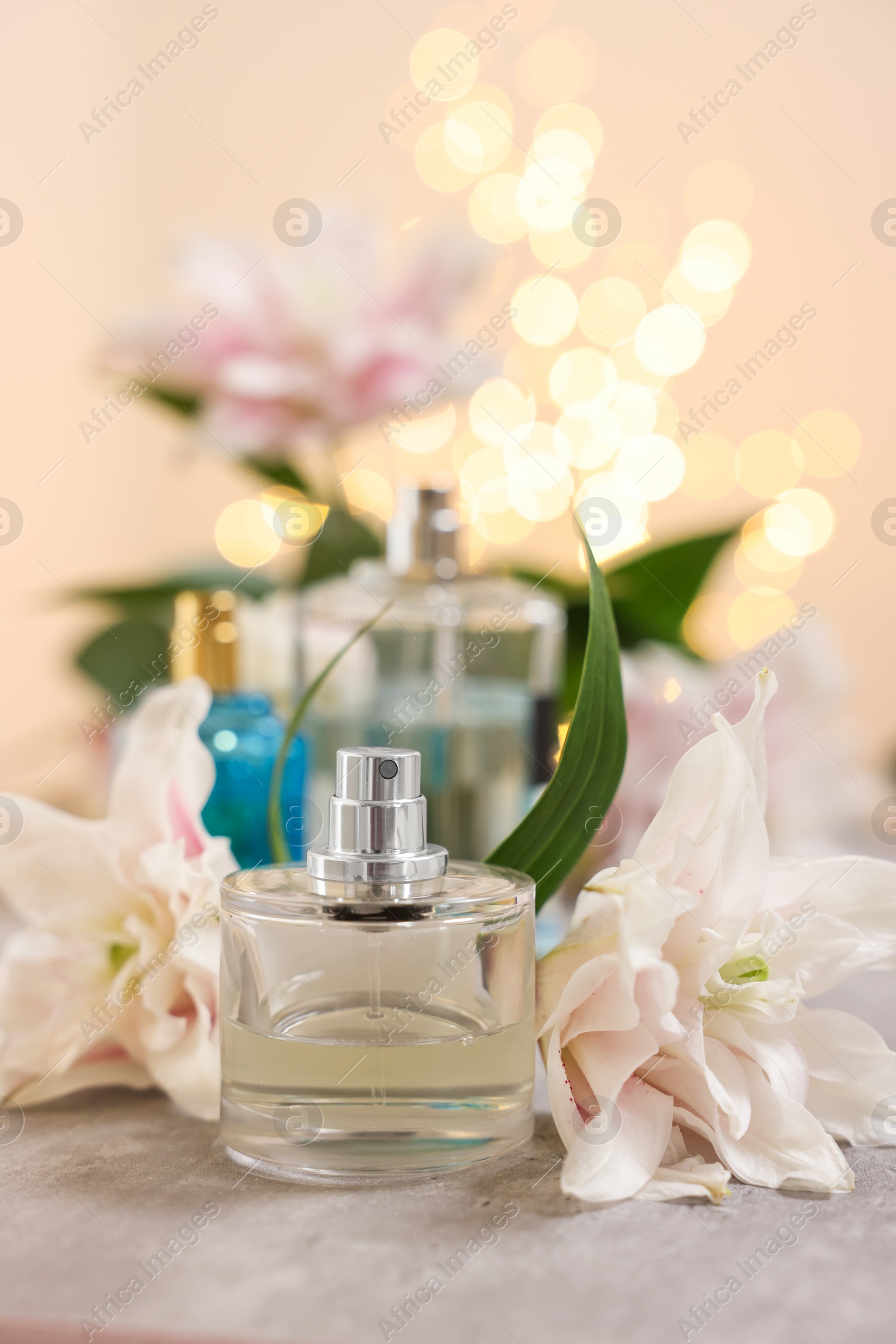 Photo of Bottles of perfume and beautiful lily flowers on table against beige background with blurred lights, closeup