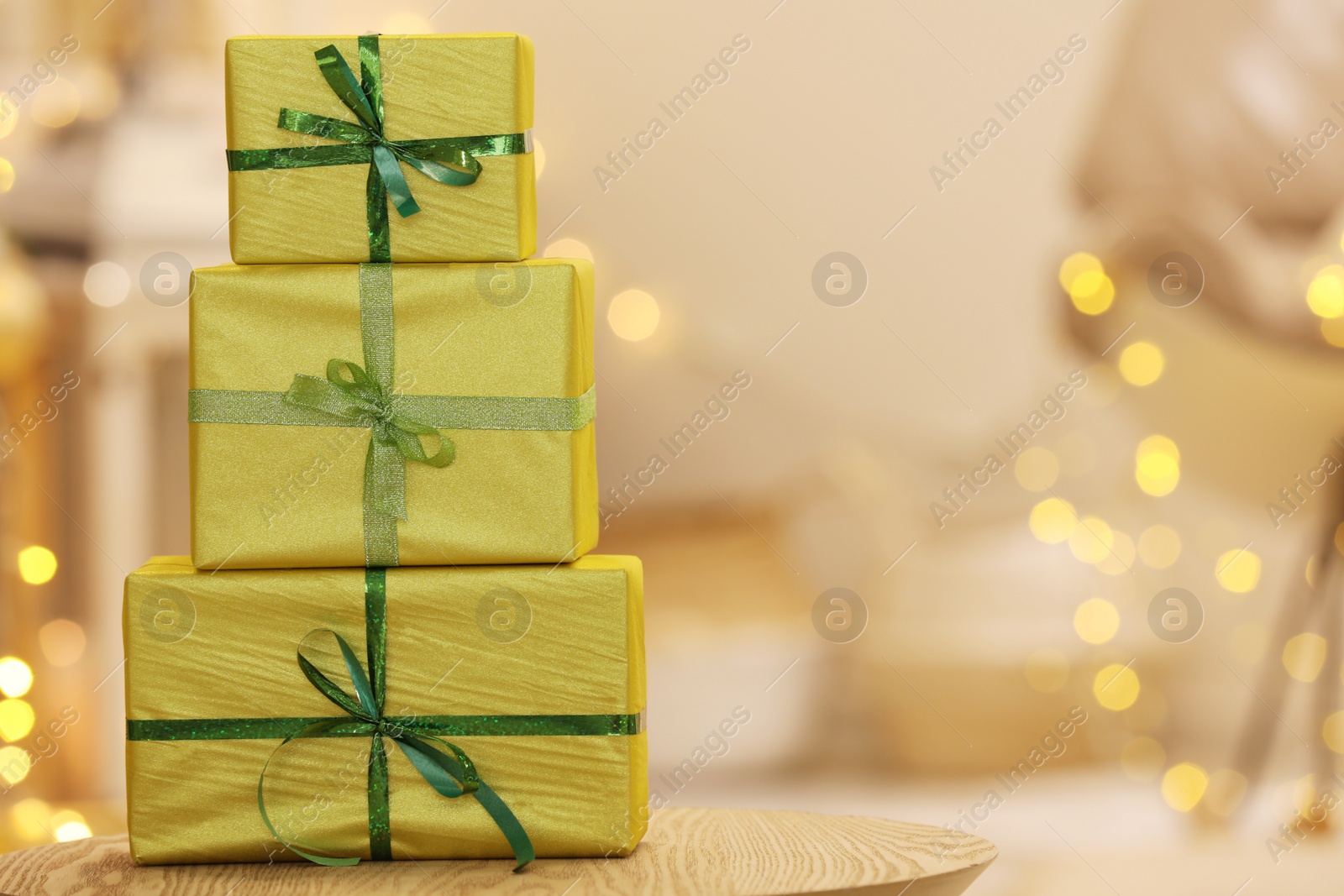 Photo of Beautifully wrapped gift boxes on wooden table against blurred festive lights, space for text. Christmas celebration