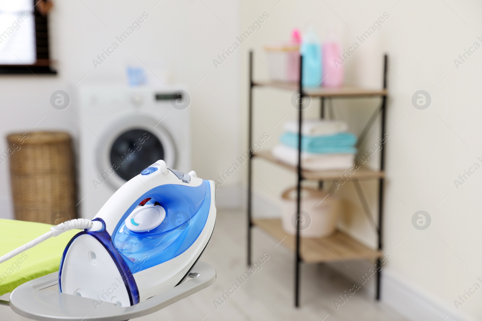Photo of Modern clothes iron on board in laundry room