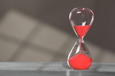 Hourglass with red flowing sand on table against light grey background, space for text