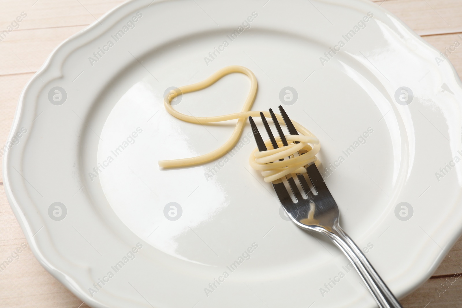 Photo of Heart made of tasty spaghetti and fork on table, closeup