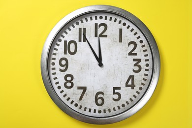 Photo of Clock showing five minutes until midnight on yellow background. New Year countdown