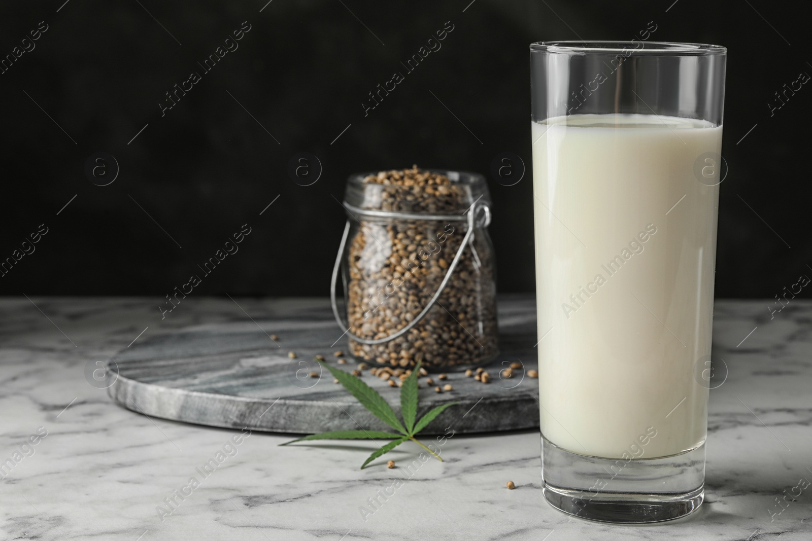 Photo of Composition with glass of hemp milk on marble table against black background. Space for text