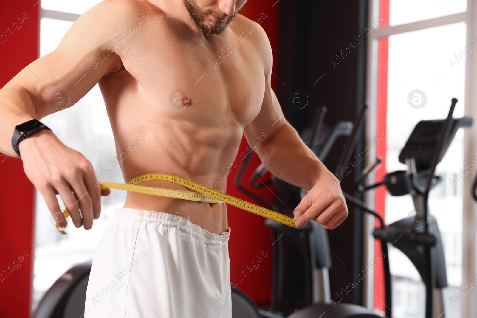 Photo of Athletic man measuring waist with tape in gym, closeup