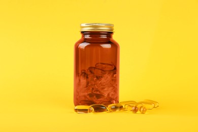 Photo of Jar with vitamin capsules on yellow background