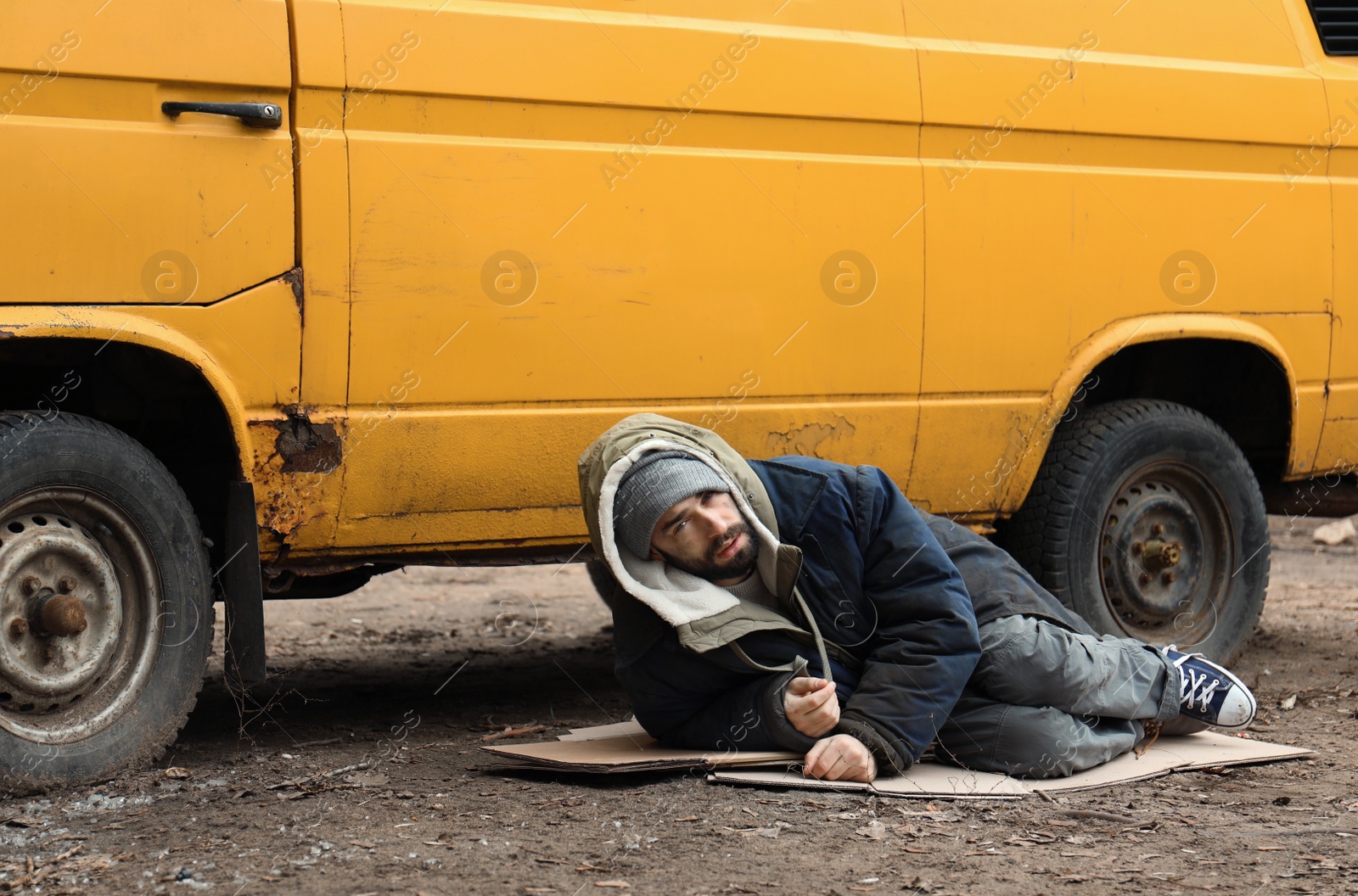 Photo of Poor homeless man lying near van outdoors