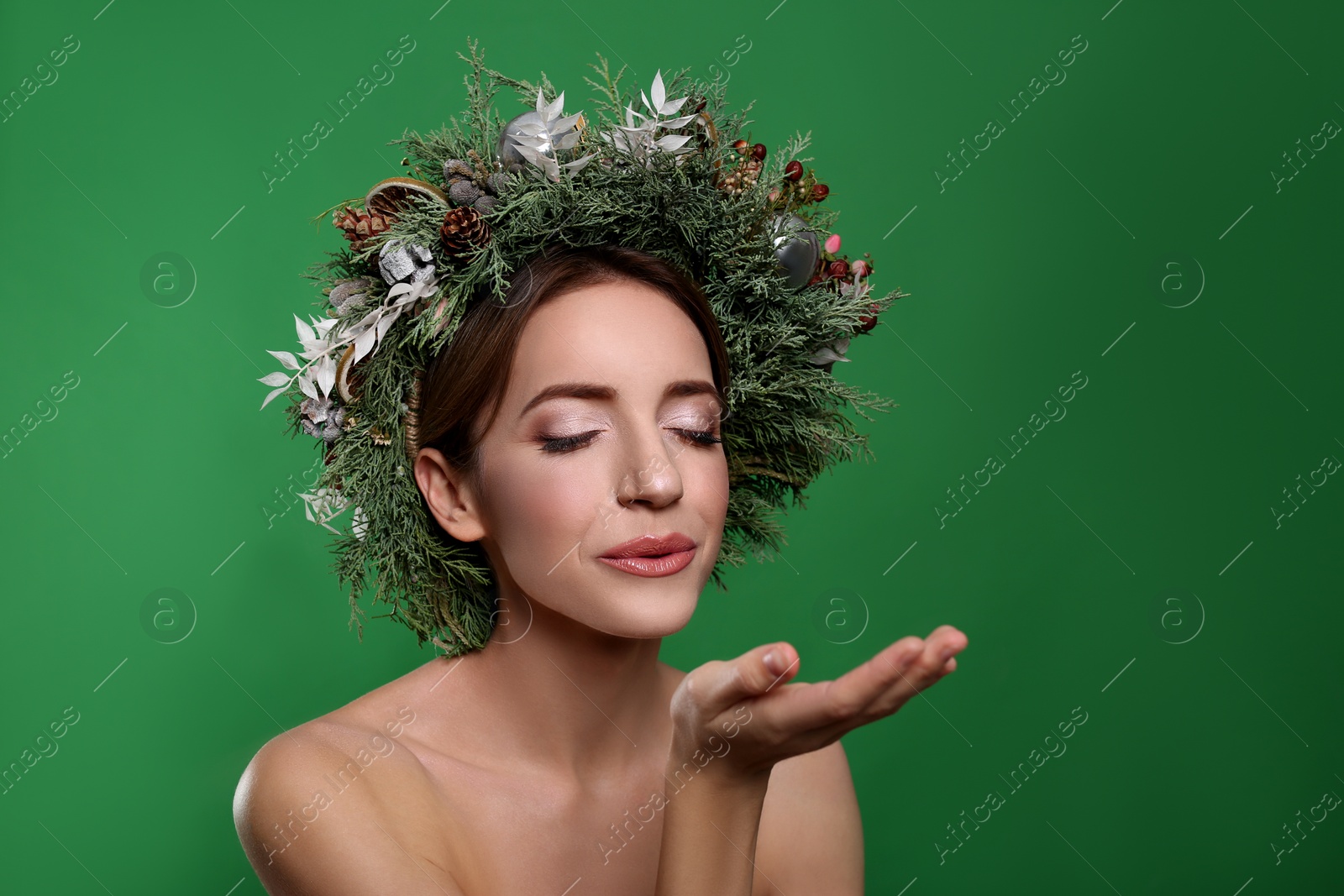 Photo of Beautiful young woman with Christmas wreath blowing kiss on green background