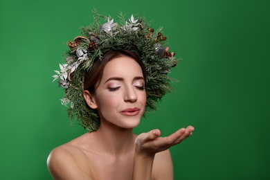 Photo of Beautiful young woman with Christmas wreath blowing kiss on green background