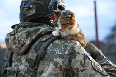 Photo of Little stray cat on Ukrainian soldier's shoulder outdoors, closeup