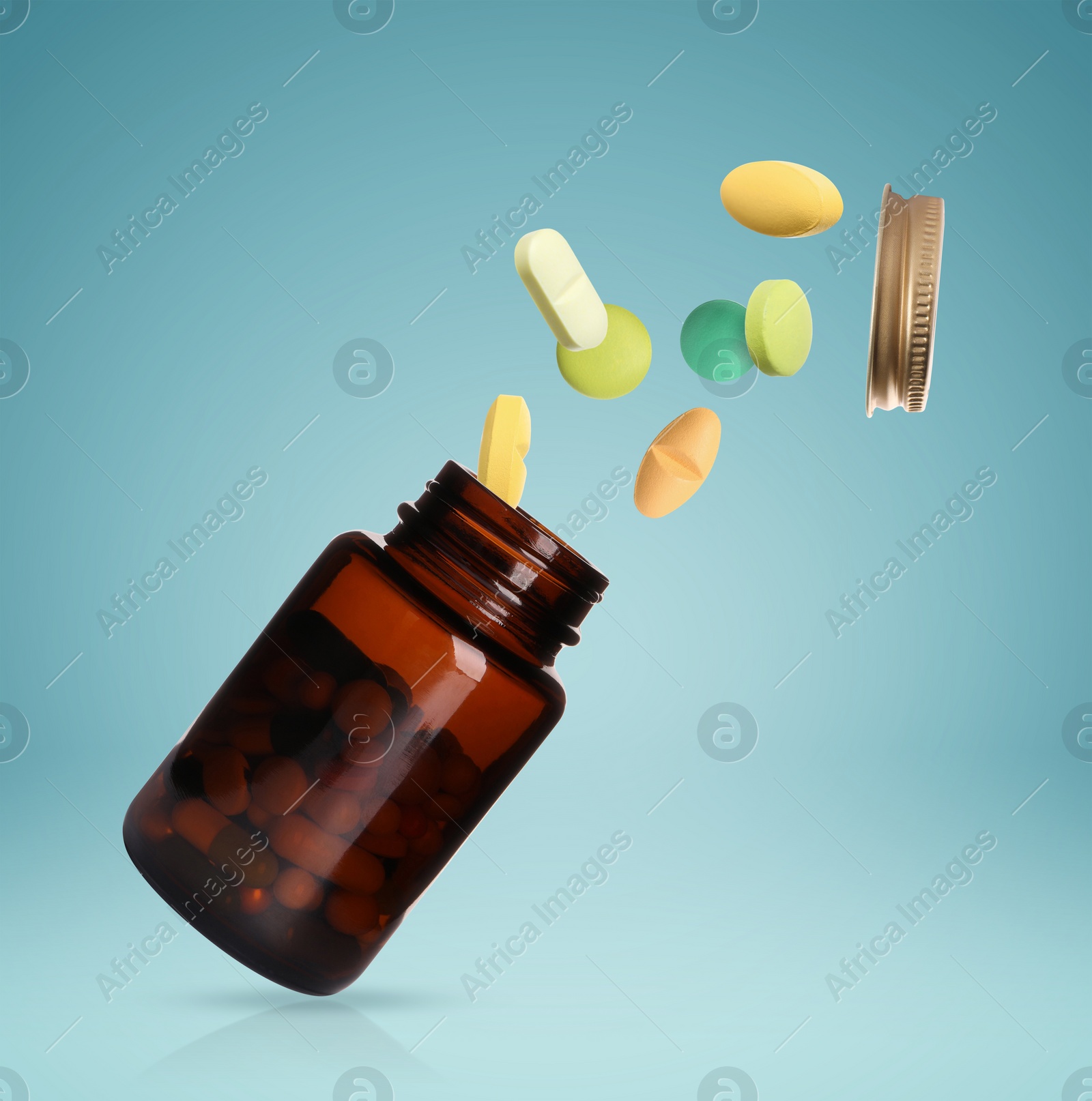 Image of Many different colorful pills bursting out of bottle on light blue background